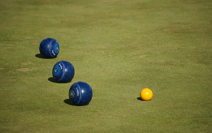 Three lawn bowls resting close to the jack on a sunlit green